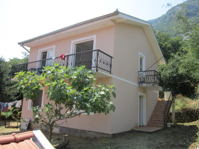 Zweistöckiges Haus mit Balkonen und Außentreppe in Kotor, Montenegro, vor Bergkulisse und grünem Garten.