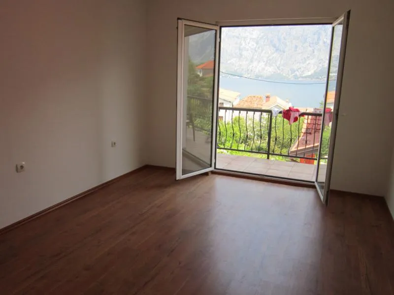 Leeres Schlafzimmer mit Laminatboden und Zugang zum Balkon mit Panoramablick auf die Bucht von Kotor, Montenegro.
