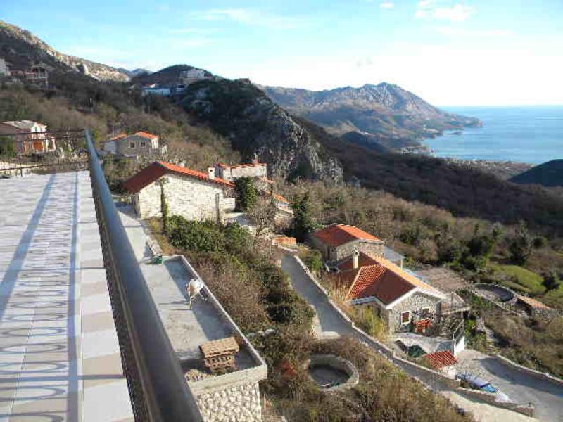 Blick von der Terrasse eines Hauses in Budva, Montenegro: Panorama der Berge, steinerne Villen mit Ziegeldächern und Meeresbucht.