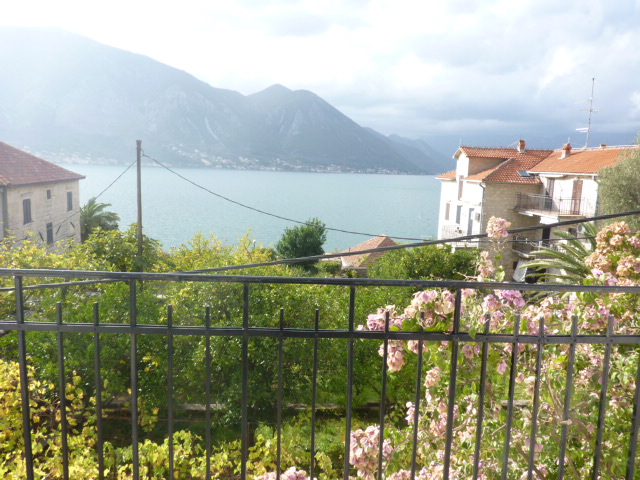 Blick vom Balkon eines Hauses in Kumbor, Montenegro: Panorama auf die Bucht von Kotor, Berge und einen blühenden Garten von der Terrasse.
