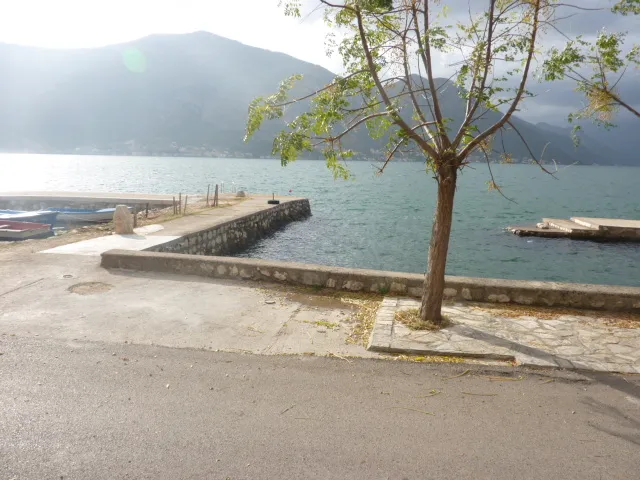 Вид на море и частный причал у дома в Кумборе, Черногория: набережная с деревом и горный пейзаж на фоне.