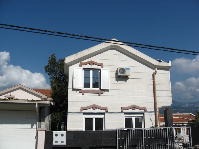 Zweistöckiges Haus in Tivat, Montenegro: helle Fassade, weiße Fensterläden, Klimaanlage und moderner Zaun.