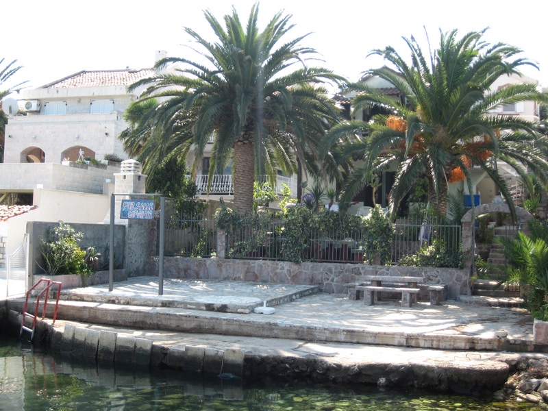 Zweistöckiges Haus in Tivat, Montenegro, mit privatem Steg, Steinterrasse, Palmen und Zugang zum Meer.
