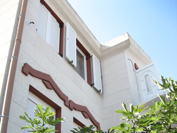 Fassade eines Hauses in Tivat, Montenegro: helle Fassade, weiße Fensterläden und dekorative Elemente im mediterranen Stil.