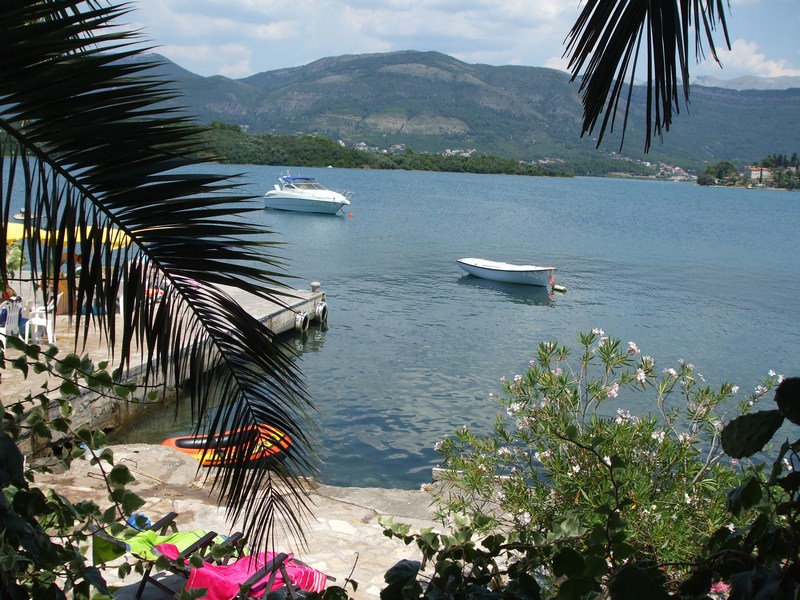 Blick auf das Meer und den Steg vom Privatstrand des Hauses in Tivat, Montenegro: Palmen, Boote und Berge im Hintergrund.