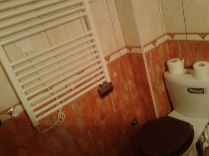 Badezimmer in einer Wohnung in Igalo, Montenegro: weiße Sanitärkeramik, Handtuchheizkörper und Wandverkleidung mit orangefarbenen Fliesen.