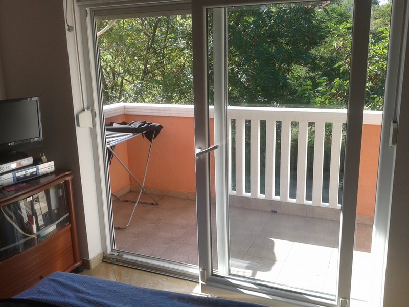 Schlafzimmer mit Zugang zum Balkon in einer Wohnung in Igalo, Montenegro: Panoramatür, Blick ins Grüne und geflieste Terrasse.