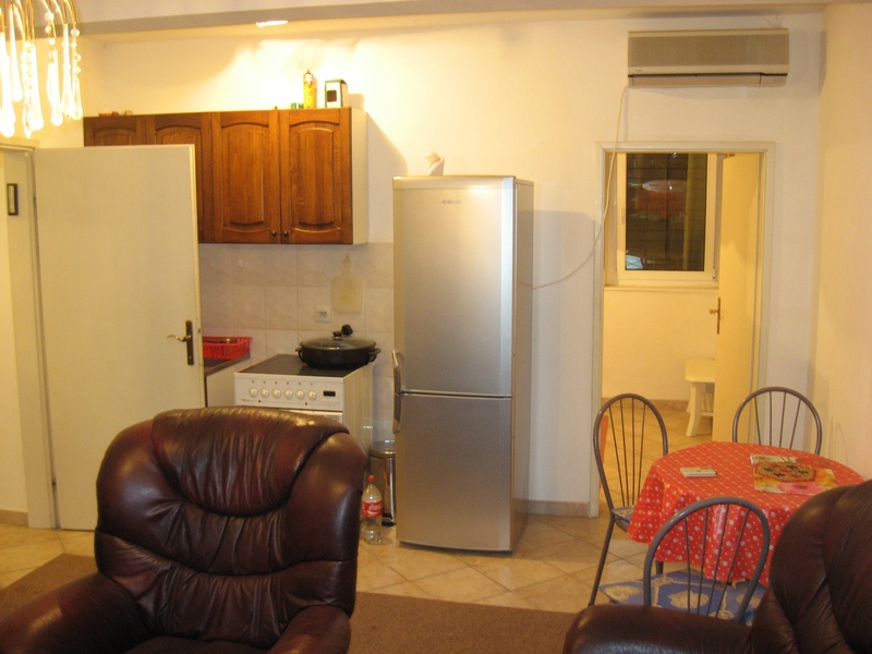 Küche in einer Wohnung in Budva, Montenegro: Holzschränke, Herd, Kühlschrank, Essbereich und Ledersessel.