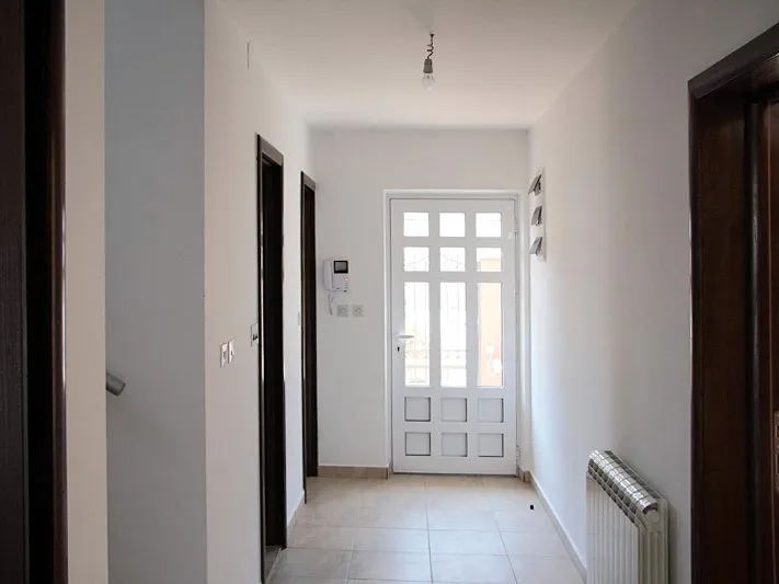Heller Flur in einem Haus in Krašići, Montenegro: weiße Wände, Fliesenboden, Heizkörper und Eingangstür mit Glas.
