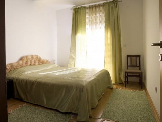 Bright bedroom with a double bed and green curtains in an apartment for sale, Zelenika, Montenegro.