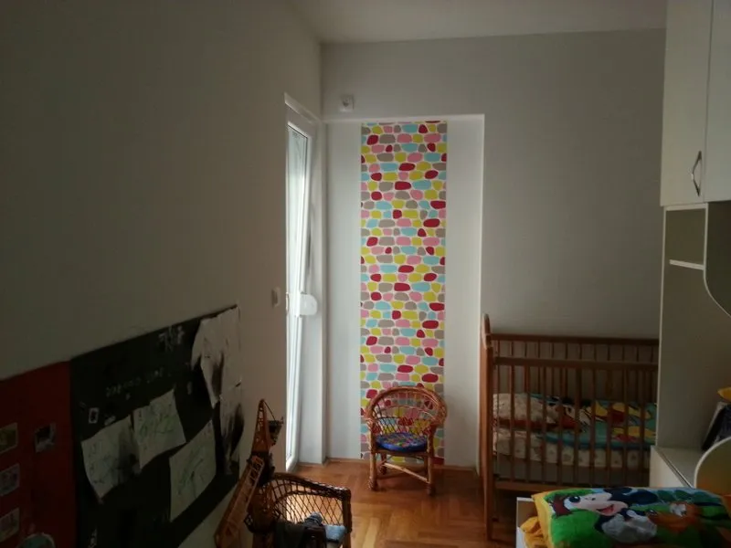 Kinderzimmer in einer Wohnung in Budva, Montenegro: Holzbettchen, geflochtener Sessel und bunte Tapete mit Muster.