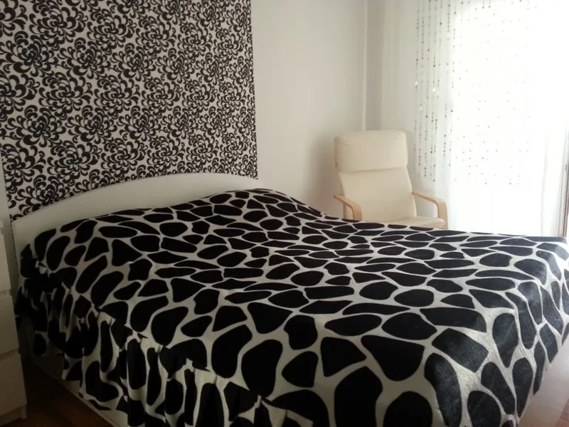 Schlafzimmer in einer Wohnung in Budva, Montenegro: Doppelbett mit schwarz-weißer Tagesdecke, Akzentwand und Sessel.
