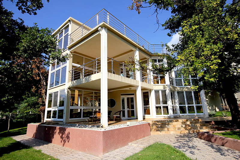 Modernes mehrstöckiges Haus mit großen Fenstern, Balkonen und einer Terrasse im Grünen.