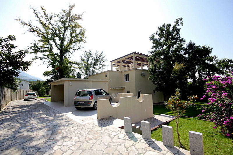 Äußeres einer modernen Villa mit Auto, Garage und Steineinfahrt im Grünen.