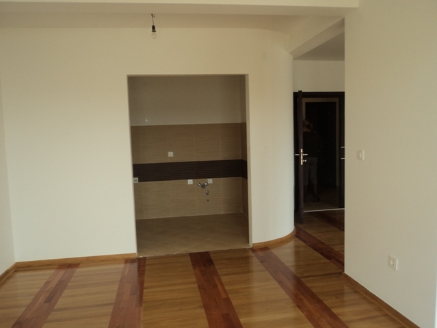 Wohnzimmer mit Parkett und Küchenbereich in einer zum Verkauf stehenden Wohnung in Bečići, Montenegro. Helle Ausstattung und modernes Design.