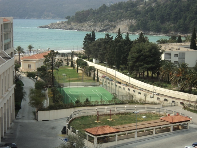 Blick auf den Tennisplatz, die Parkanlage und das Meer von der Wohnung in Bečići, Montenegro. Wohnanlage mit Infrastruktur.