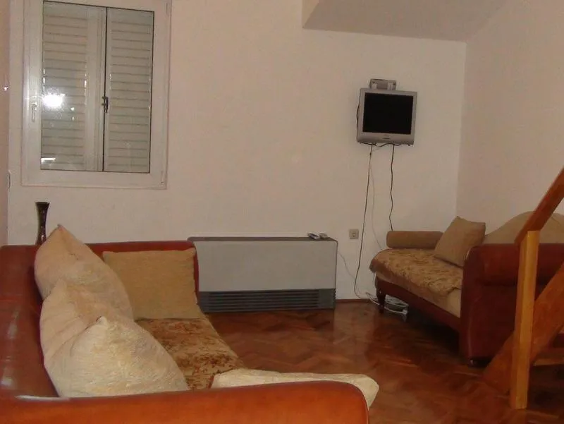 Wohnzimmer in einer Wohnung in Budva, Montenegro: Ledersofas, Parkettboden, Fernseher und Fenster mit Jalousien.