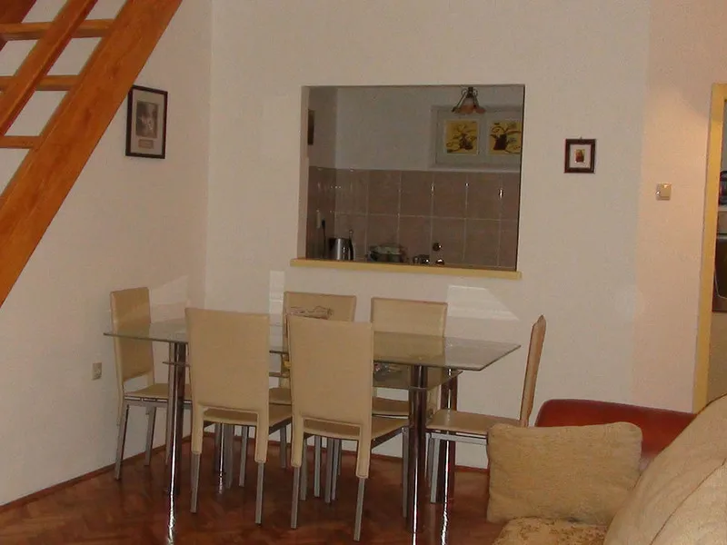 Wohnzimmer mit Essbereich und Holztreppe in einer Wohnung in Budva, Montenegro: Glastisch und helle Stühle.