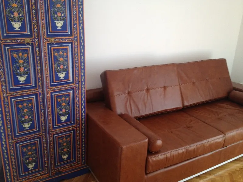 Innenansicht des Wohnzimmers in einer Wohnung in Budva, Montenegro: braunes Ledersofa und heller Schrank mit ethnischer Bemalung.