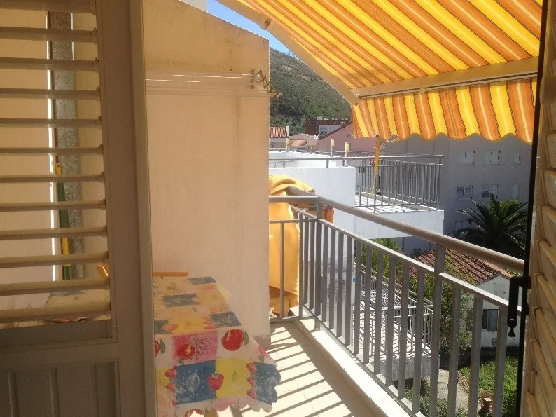 Balkon einer Wohnung in Budva, Montenegro: Blick auf die Berge, gestreifte Sonnenmarkise, Tisch mit bunter Tischdecke und Geländer.