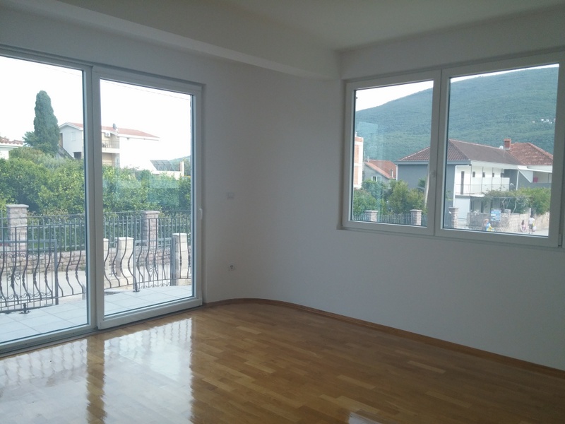 Svetla dnevna soba sa panoramskim prozorima i pogledom na planine u kući u Đenovićima, Crna Gora, parketni pod i izlaz na terasu
