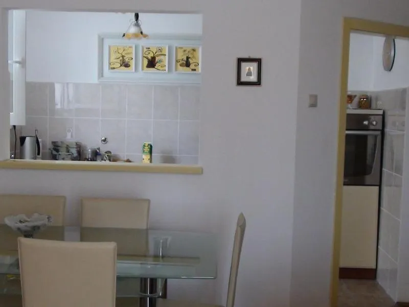 Innenraum des Wohnzimmers mit Essbereich und Durchgang zur Küche in einer Wohnung, Budva, Montenegro: Glastisch und helle Stühle.