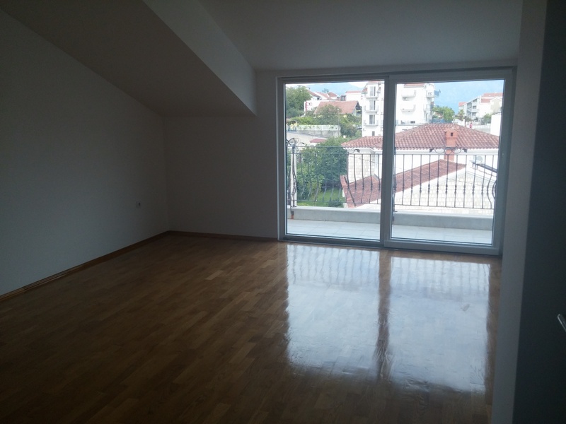 Svetla dnevna soba sa parketom i izlazom na balkon u kući u Đenovićima, Crna Gora, pogled na grad i planine.