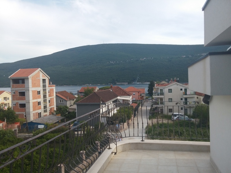 Pogled sa prostranog balkona kuće u Đenovićima, Crna Gora: panorama mora, planina i prijatnih gradskih zgrada.