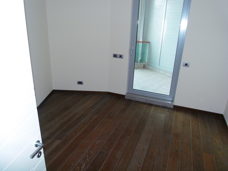 Helles Schlafzimmer mit dunklem Parkett und Zugang zum Balkon in einer Wohnung, Stadt Budva, Montenegro.