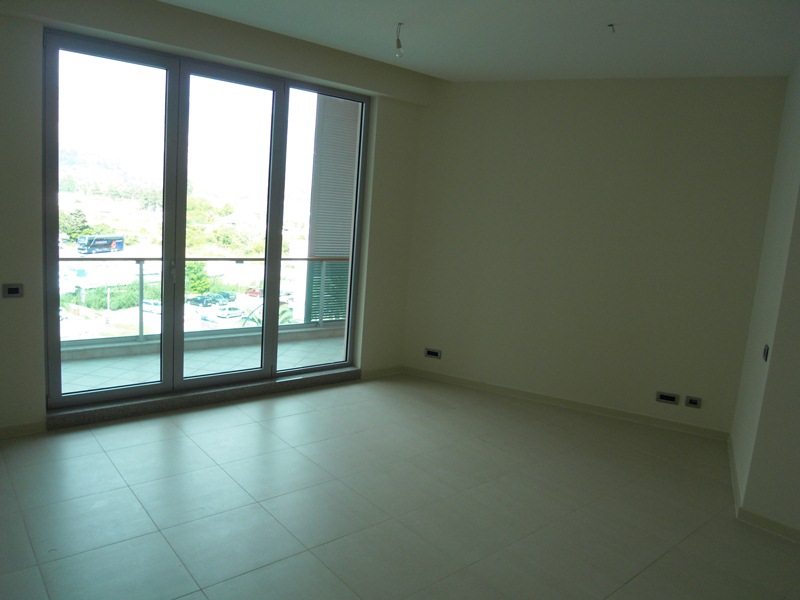 Helles Wohnzimmer in einer neuen Wohnung in Budva, Montenegro, mit Panoramafenstern, Zugang zum Balkon und Fliesenboden.