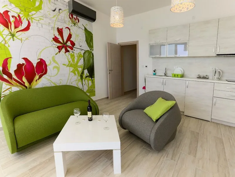 Wohnzimmer kombiniert mit einer Küche, grünem Sofa, grauem Sessel und weißem Couchtisch.