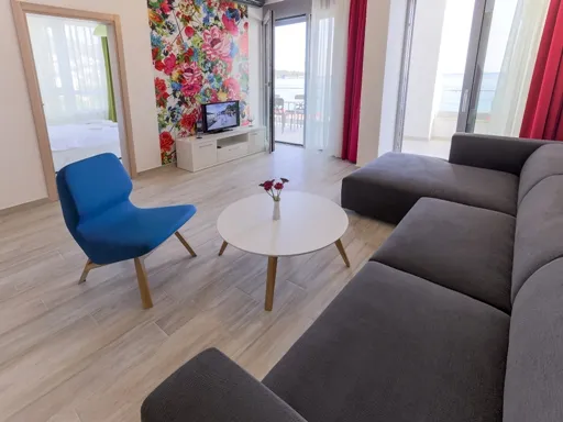 Modernes Wohnzimmer mit dunkelgrauem Sofa, blauem Sessel, weißem Couchtisch, TV und Balkonblick.
