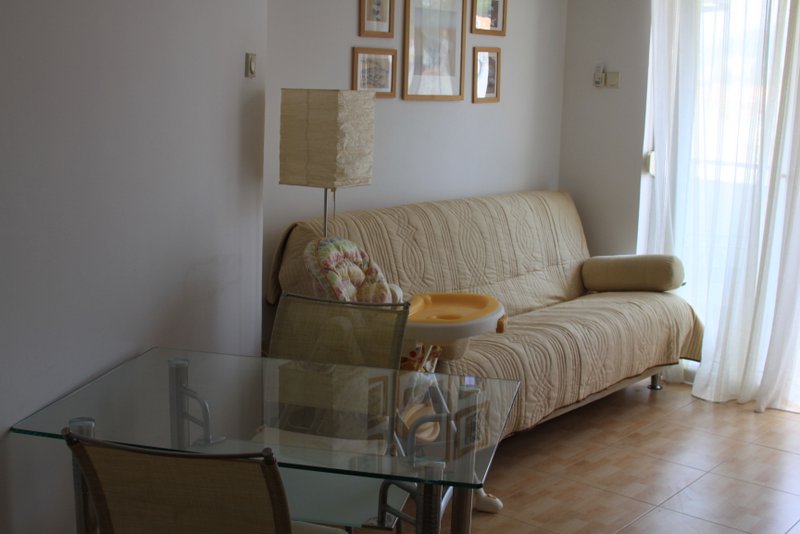 Udoban dnevni boravak u stanu u Rafailovićima, Crna Gora: stakleni sto, bež sofa i izlaz na balkon.