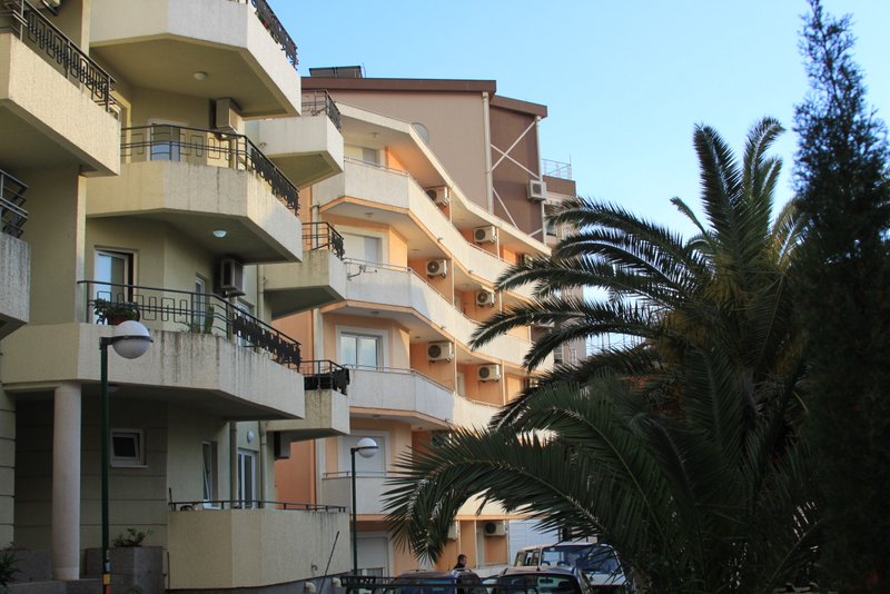 Fasada višespratne zgrade sa balkonima i palmama u Rafailovićima, Crna Gora, pogled na stambeni kompleks spolja.