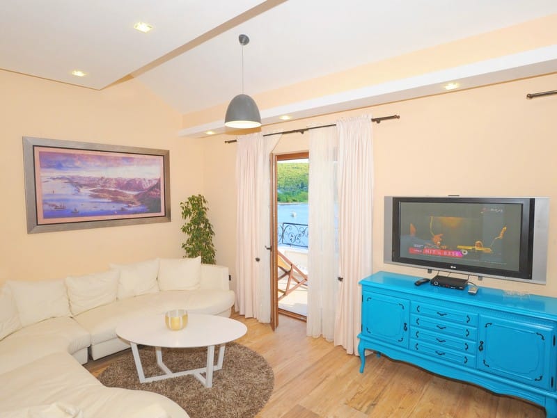 Living room in a villa in Bigovo, Montenegro: white sofa, bright blue cabinet, TV, and access to a terrace with sea view.
