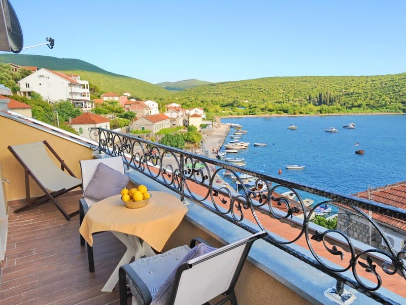 Villa balcony in Bigovo, Montenegro: sea view, pier with boats, table with lemons, and wrought-iron railing.