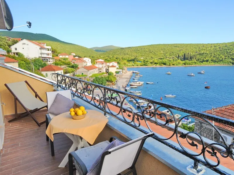 Villa balcony in Bigovo, Montenegro: sea view, pier with boats, table with lemons, and wrought-iron railing.
