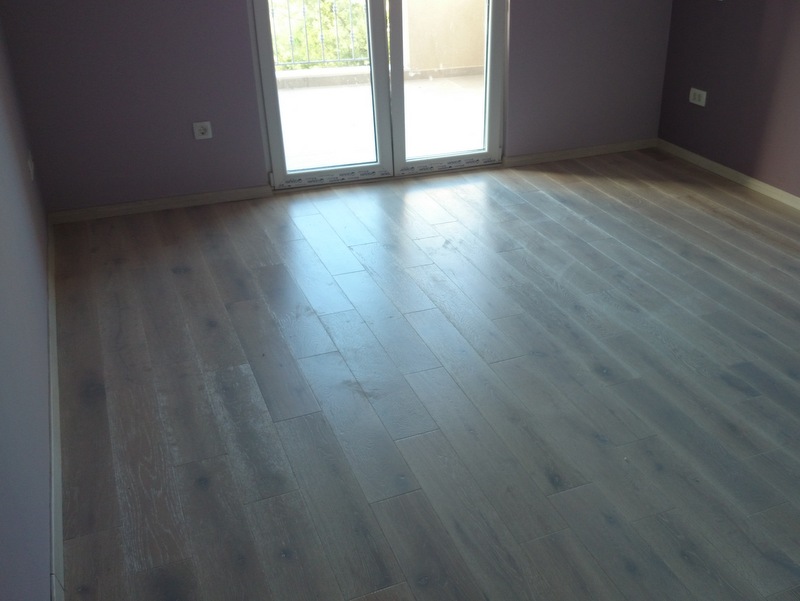 Svetla dnevna soba sa laminatom i izlazom na balkon u kući, Herceg Novi, Crna Gora. Savremena završna obrada enterijera.