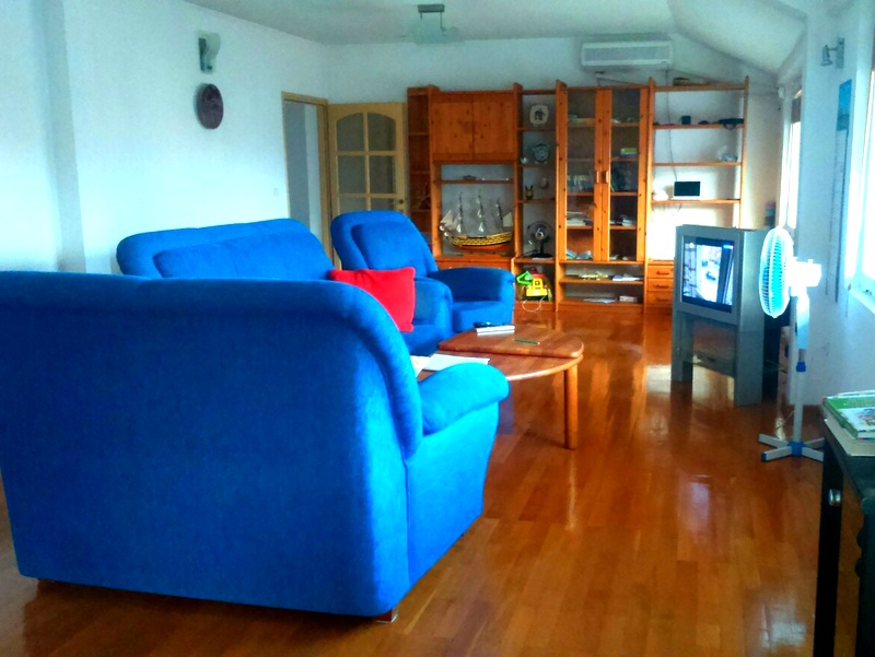 Wohnzimmer in einer Wohnung in Budva, Montenegro: blaue Sofas, Holzboden, Regal und Fernseher im Interieur.