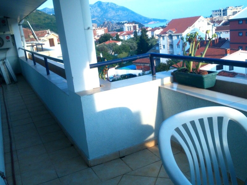 Geräumiger Balkon der Wohnung in Budva, Montenegro, mit Blick auf Berge, Stadt und Meer, Kunststoffmöbel und Blumen.