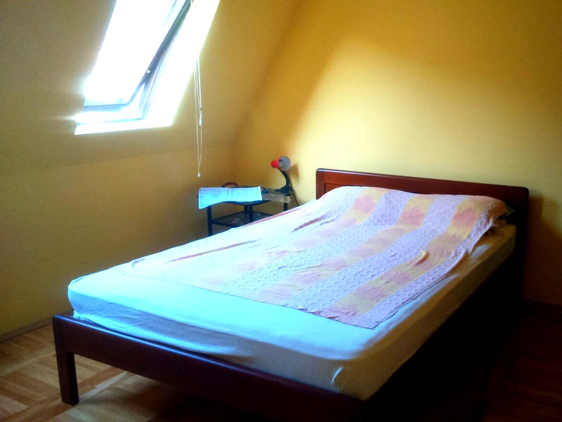 Schlafzimmer mit Doppelbett und Dachfenster in einer Wohnung, Budva, Montenegro. Gelbe Wände und Parkettboden.