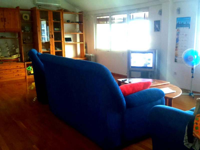 Wohnzimmer in einer Wohnung in Budva, Montenegro: blaues Sofa, Holzmöbel, Parkettboden und Fernseher am Fenster.