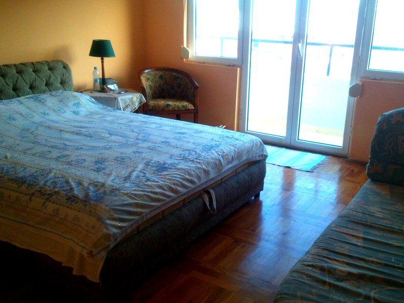Schlafzimmer in einer Wohnung in Budva, Montenegro: Doppelbett, Parkettboden, Zugang zum Balkon und ein Sessel.