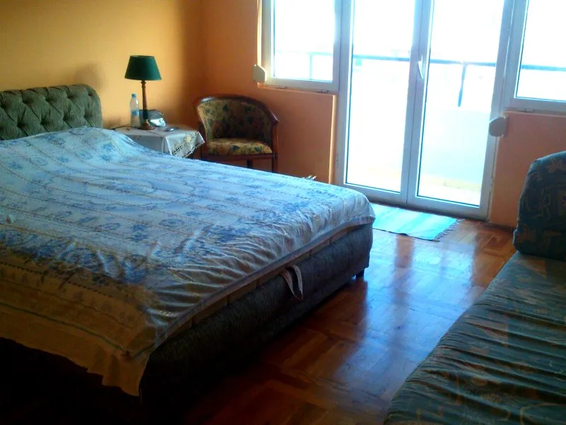 Schlafzimmer in einer Wohnung in Budva, Montenegro: Doppelbett, Parkettboden, Zugang zum Balkon und ein Sessel.