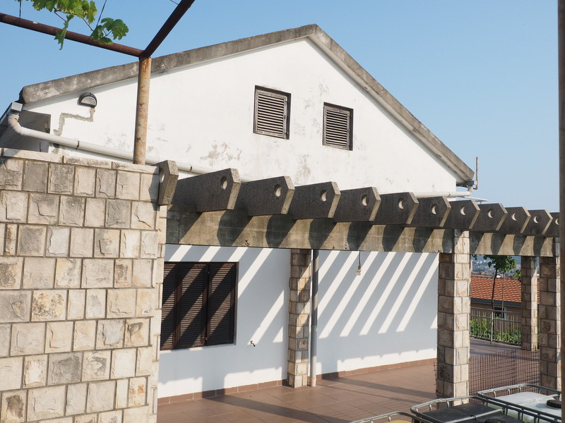 White house with a stone terrace and pergola in Shushan, Montenegro: view of the facade and outdoor relaxation area.