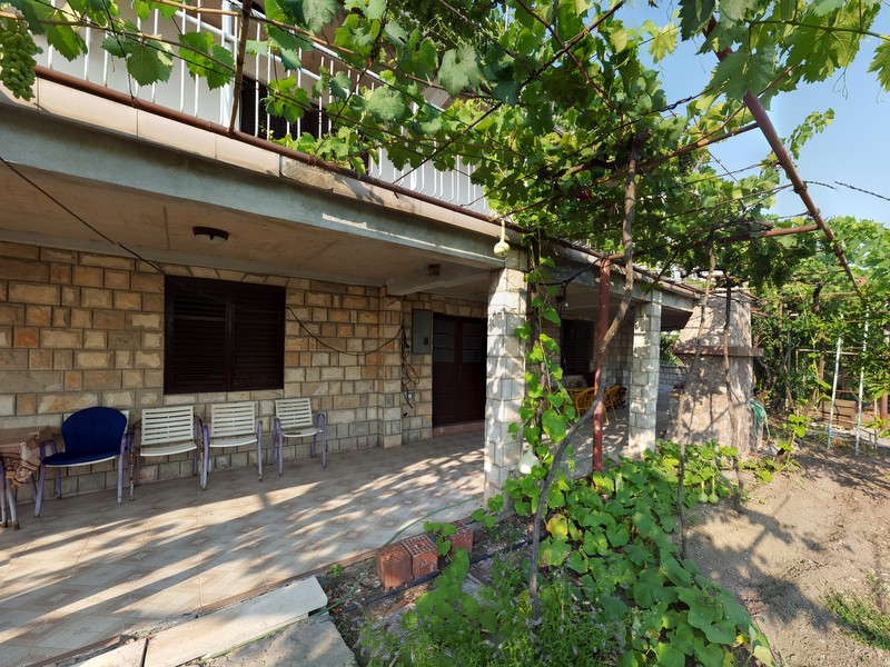 Terrace of a house in Shushan, Montenegro: stone facade finish, garden furniture, and a vineyard above the seating area.