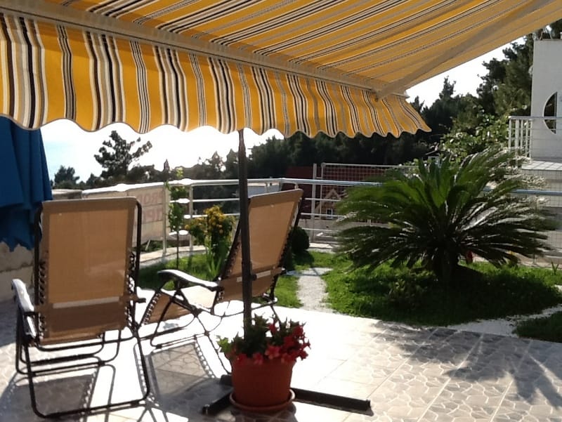 House terrace in Shushan, Montenegro: sun loungers, striped awning, sea view, and a well-kept garden with a palm tree.