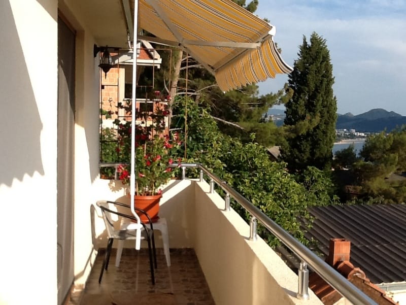 Balcony with an awning and sea view in a house in Shushan, Montenegro: chairs, potted flowers, and a panoramic landscape.