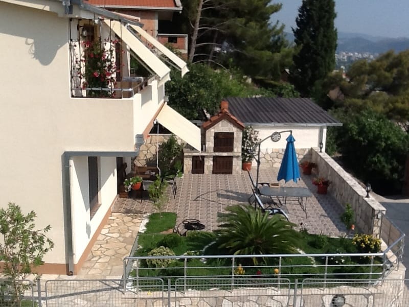 House in Shushan, Montenegro: terrace with a stone barbecue, garden furniture, an umbrella, and a well-kept garden with a palm tree.
