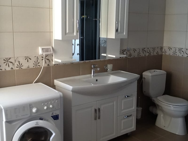 Bathroom in a house, Shushan, Montenegro: light tiles, vanity with sink, mirror, and washing machine.